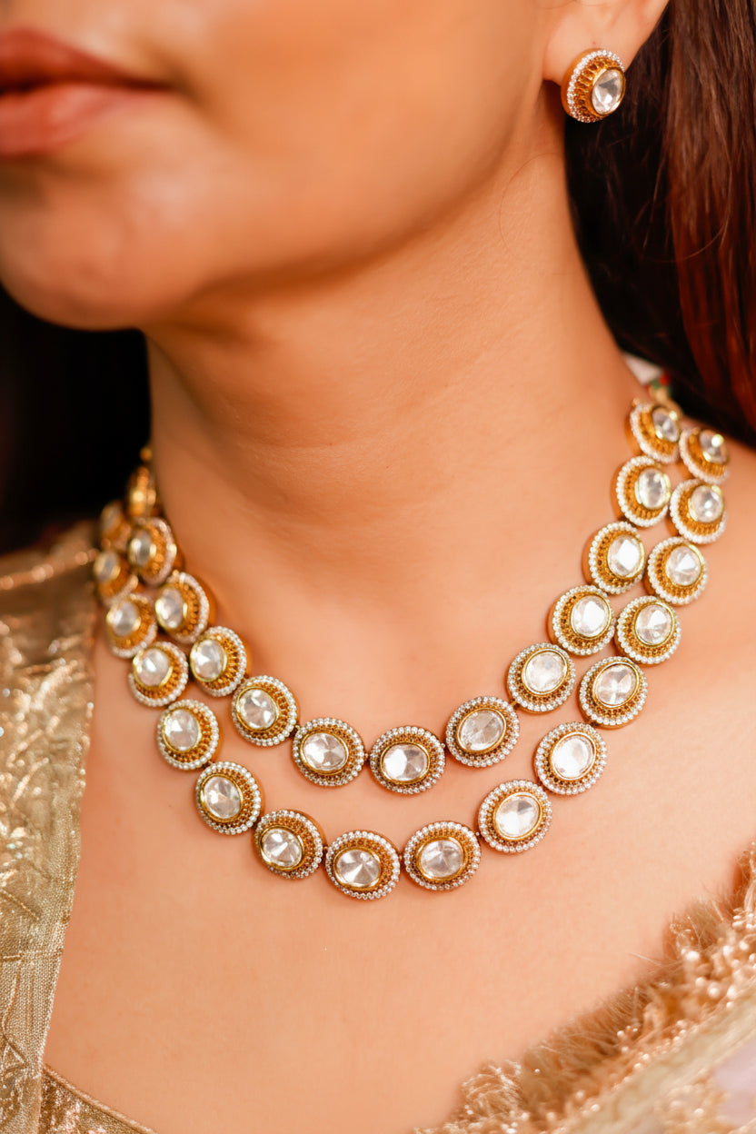 A close-up of a woman wearing a gold-toned traditional necklace with clear round stones and matching stud earrings.